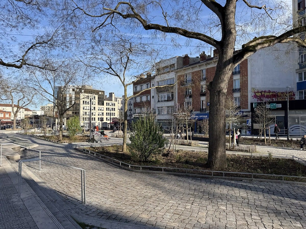 La place Jacques-Duclos réaménagée à la Croix-de-Chavaux, avec pavés, jeunes plantations et commerces en fond.