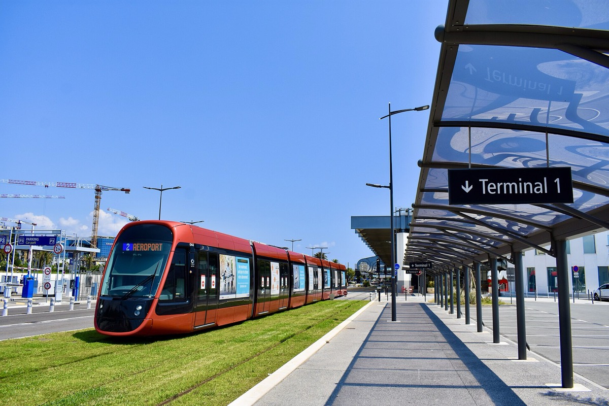 Rame du tramway ligne 2 de Nice à l'arrêt devant le terminal 1 de l'aéroport, grues de chantier en arrière-plan.